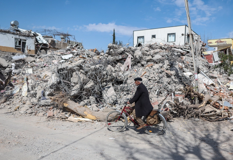 En Turquie, un homme à vélo passe devant des bâtiments détruits après le séisme – besoin d’aide d’urgence, de reconstruction et de soutien durable