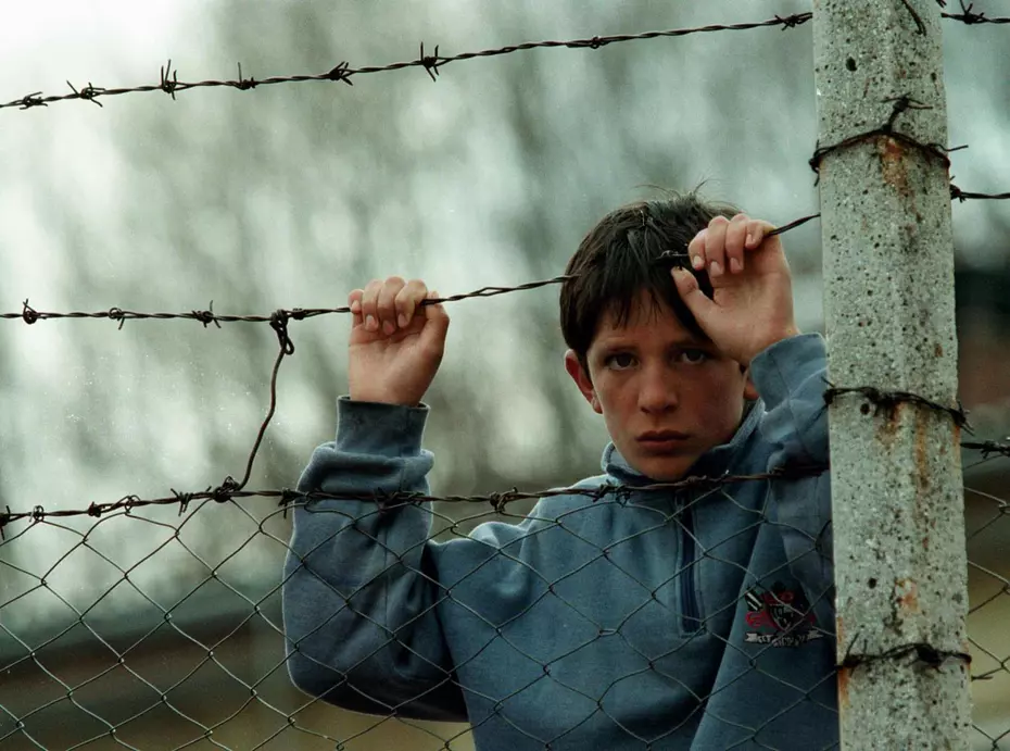 Un garçon s'accrochant à une clôture de barbelés pendant le conflit du Kosovo en 1999 - symbole de la souffrance et de l'espoir soutenu par la Chaîne du Bonheur.