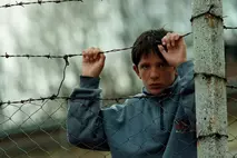Un garçon s'accrochant à une clôture de barbelés pendant le conflit du Kosovo en 1999 - symbole de la souffrance et de l'espoir soutenu par la Chaîne du Bonheur.