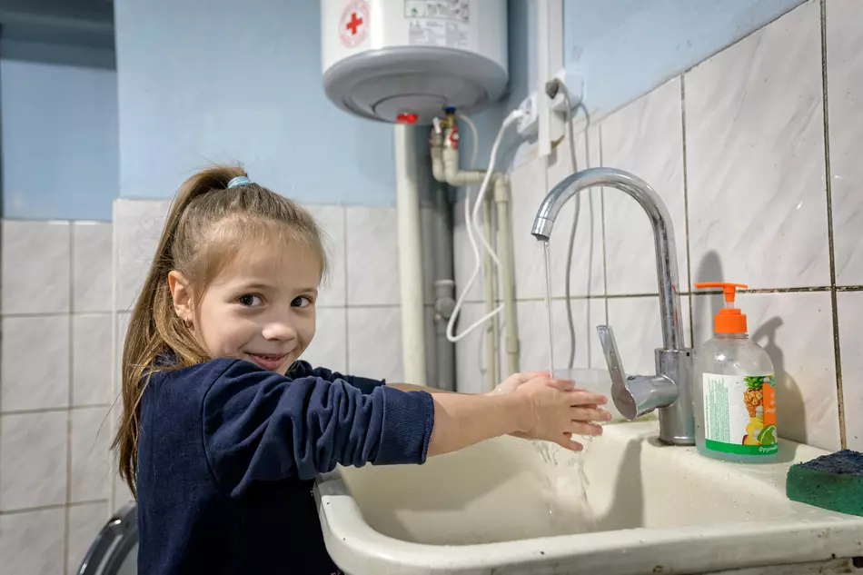 De l’eau propre pour les enfants en Ukraine Une fillette se lave les mains avec le sourire – un accès à l’eau potable et à l’hygiène rendu possible grâce à l’aide humanitaire en Ukraine.