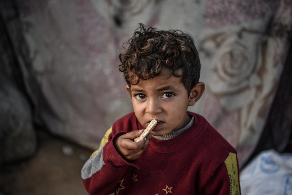 Petit garçon avec un morceau de pain Un petit garçon mange un morceau de pain – les dons permettent une aide alimentaire essentielle en temps de guerre.