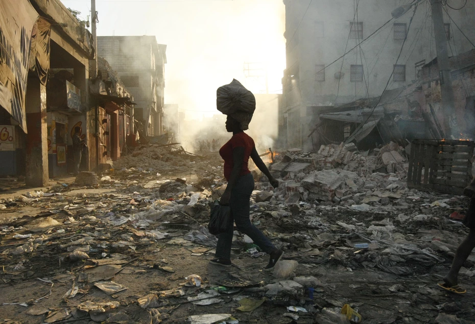 Une femme traverse une ville détruite en Haïti, un sac sur la tête, au coucher du soleil, après le tremblement de terre de 2010 soutenu par la Chaîne du Bonheur.
