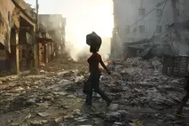 Une femme traverse une ville détruite en Haïti, un sac sur la tête, au coucher du soleil, après le tremblement de terre de 2010 soutenu par la Chaîne du Bonheur.