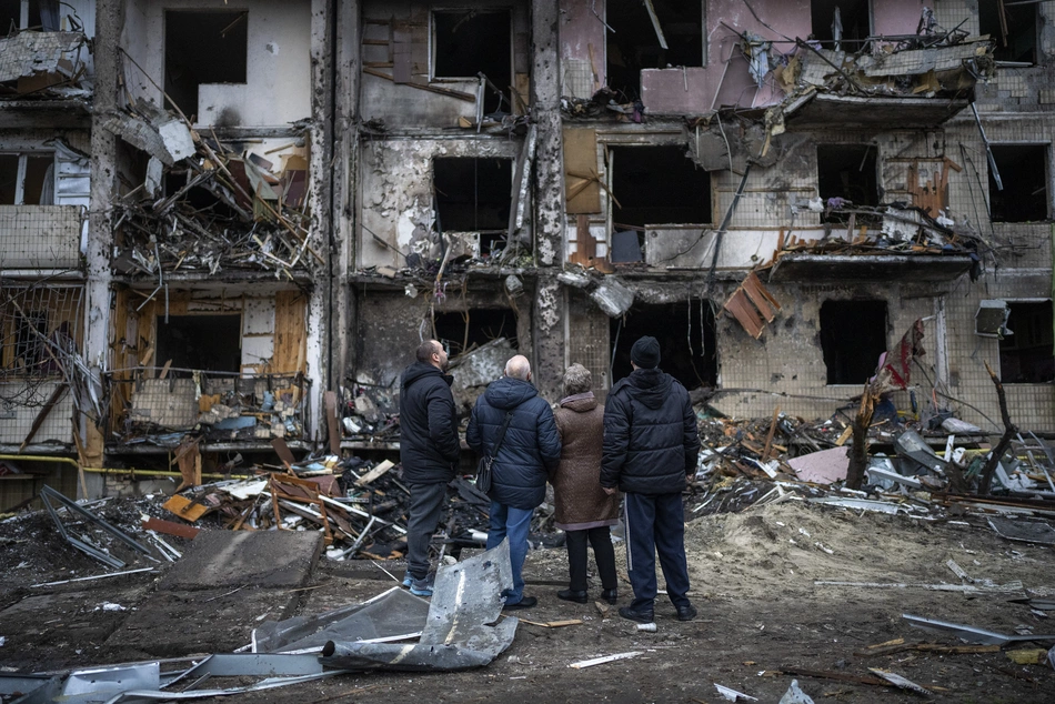 Maison détruite à Kiev Quatre personnes observent les ruines d’un immeuble gravement endommagé à Kyiv – des traces visibles de la guerre et un besoin urgent d’aide humanitaire et de reconstruction.