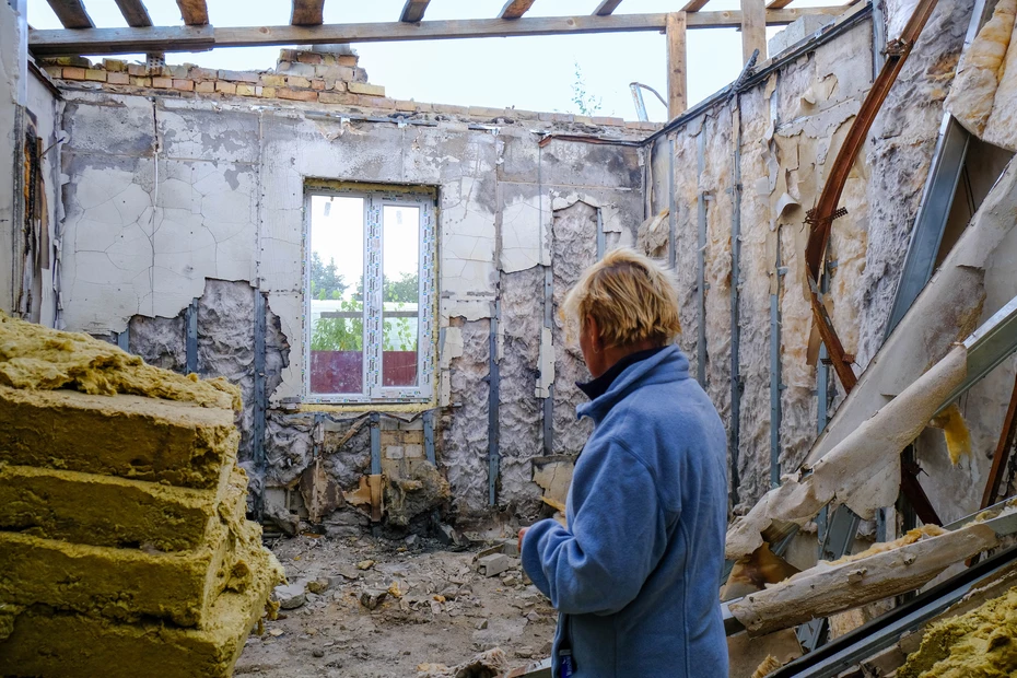 Une personne se tient à l'intérieur d'une maison bombardée en Ukraine, regardant dans une pièce détruite - symbole de l'impact de la guerre sur les civils.