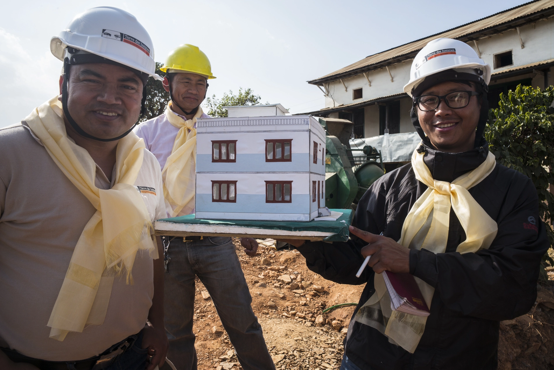 Trois hommes en casque présentent une maquette de maison pour une reconstruction sûre après catastrophe, renforçant la résilience et la protection.