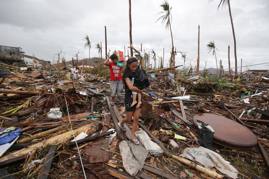 Aux Philippines, des personnes traversent les décombres après une catastrophe – un besoin urgent de soutien d’urgence, de reconstruction et de protection des plus vulnérables.