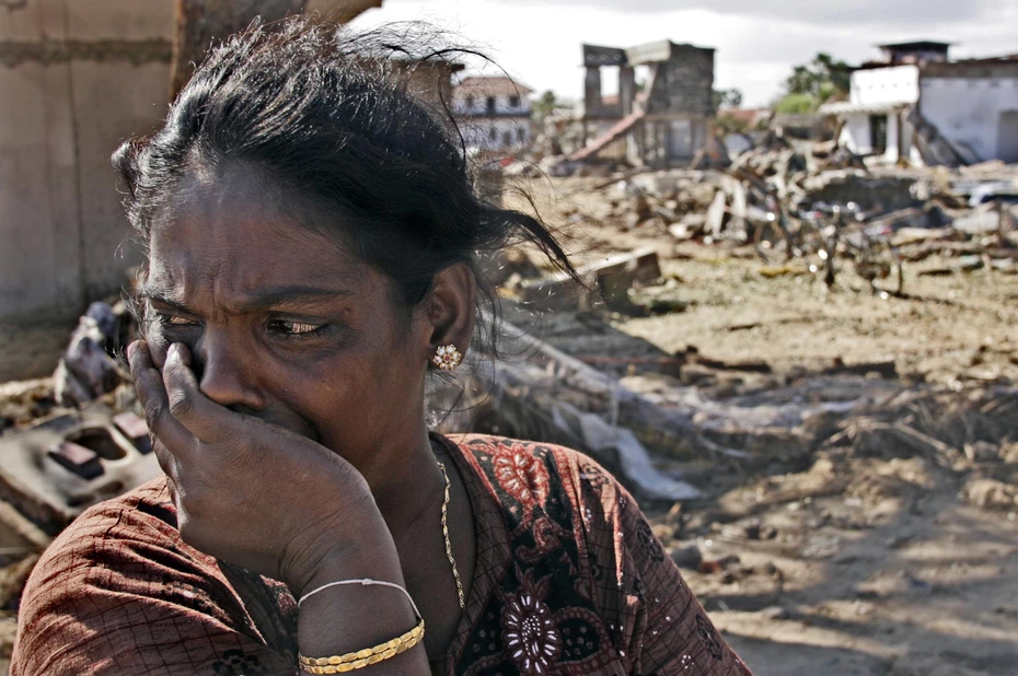 Une femme, les larmes aux yeux, regarde sur le côté, debout devant un paysage dévasté par le tsunami de 2004 en Asie du Sud-Est.