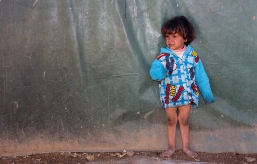 Fillette pieds nus debout sur un sol meuble, l'air anxieux - faites un don pour aider les enfants dans le besoin.