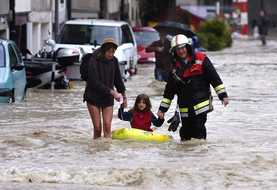  Un homme et une femme tenant les mains d'un enfant assis sur un bateau pneumatique jaune marchant dans les rues inondées lors des opérations de secours menées à la suite des inondations de 2005 en Suisse.