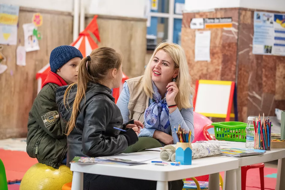Apprendre malgré la guerre Une enseignante échange avec deux enfants dans une salle d’apprentissage colorée – un accès à l’éducation pour les enfants déplacés en Ukraine malgré la guerre.