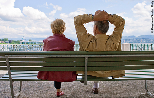 Una coppia di anziani seduta su una panchina guarda il lago.