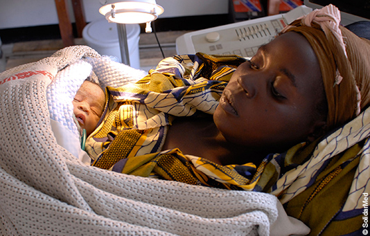 A mother lies in a hospital bed, her new-born baby in her arms.
